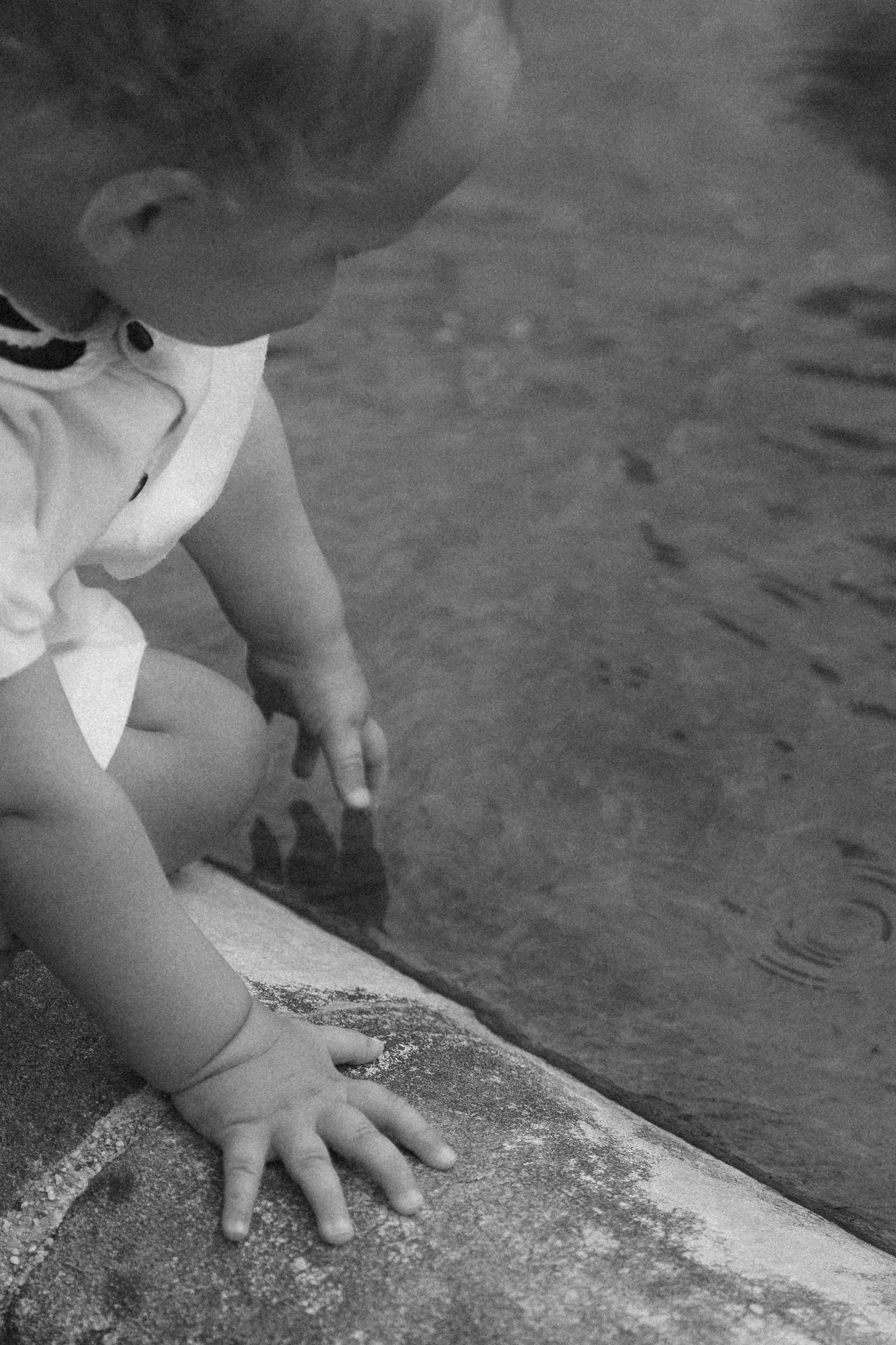 A child touching the still water of a garden pond, in black and white