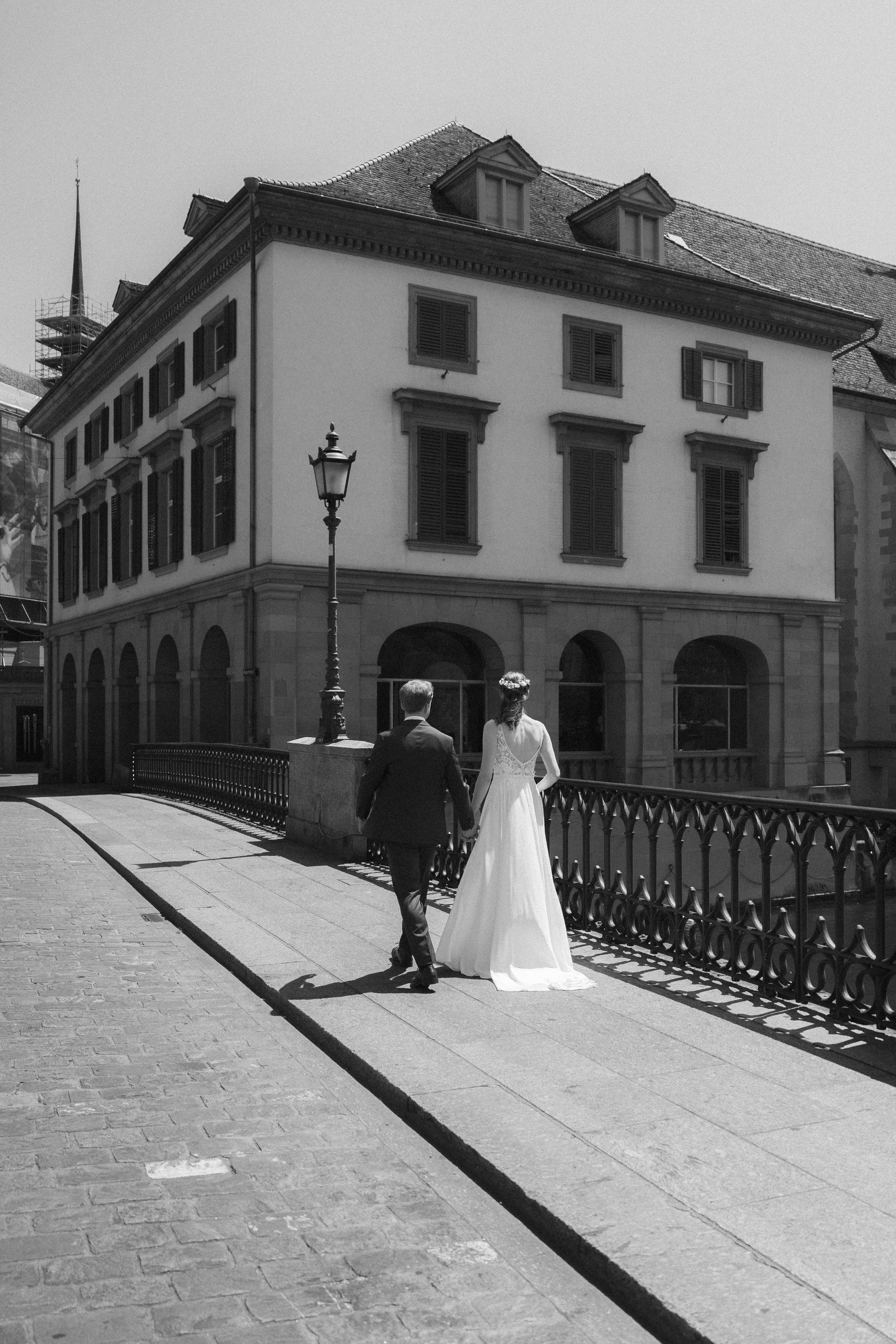 A bride and groom crossing a bridge, in black and white
