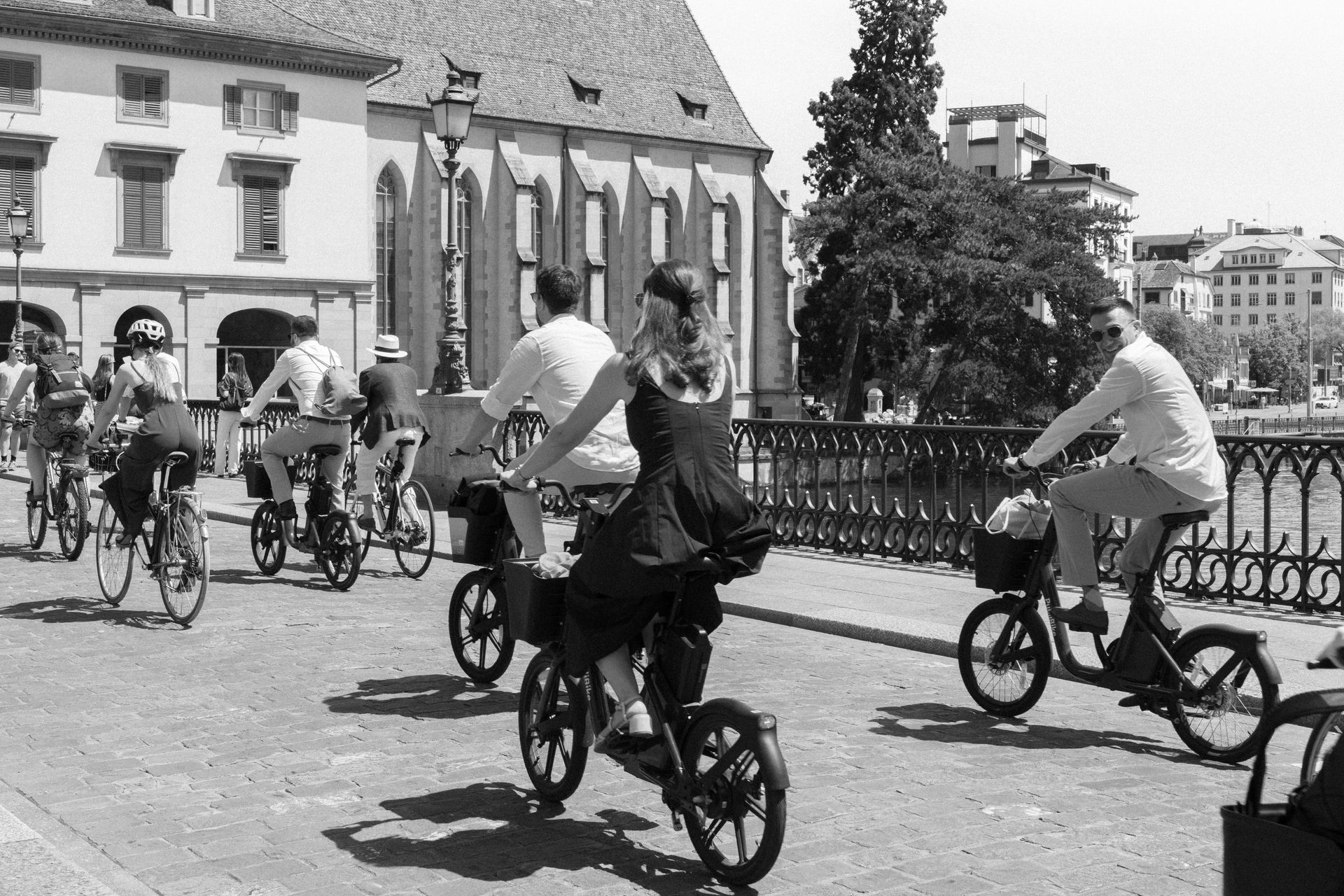 Wedding guests riding bikes across a bridge, in black and white