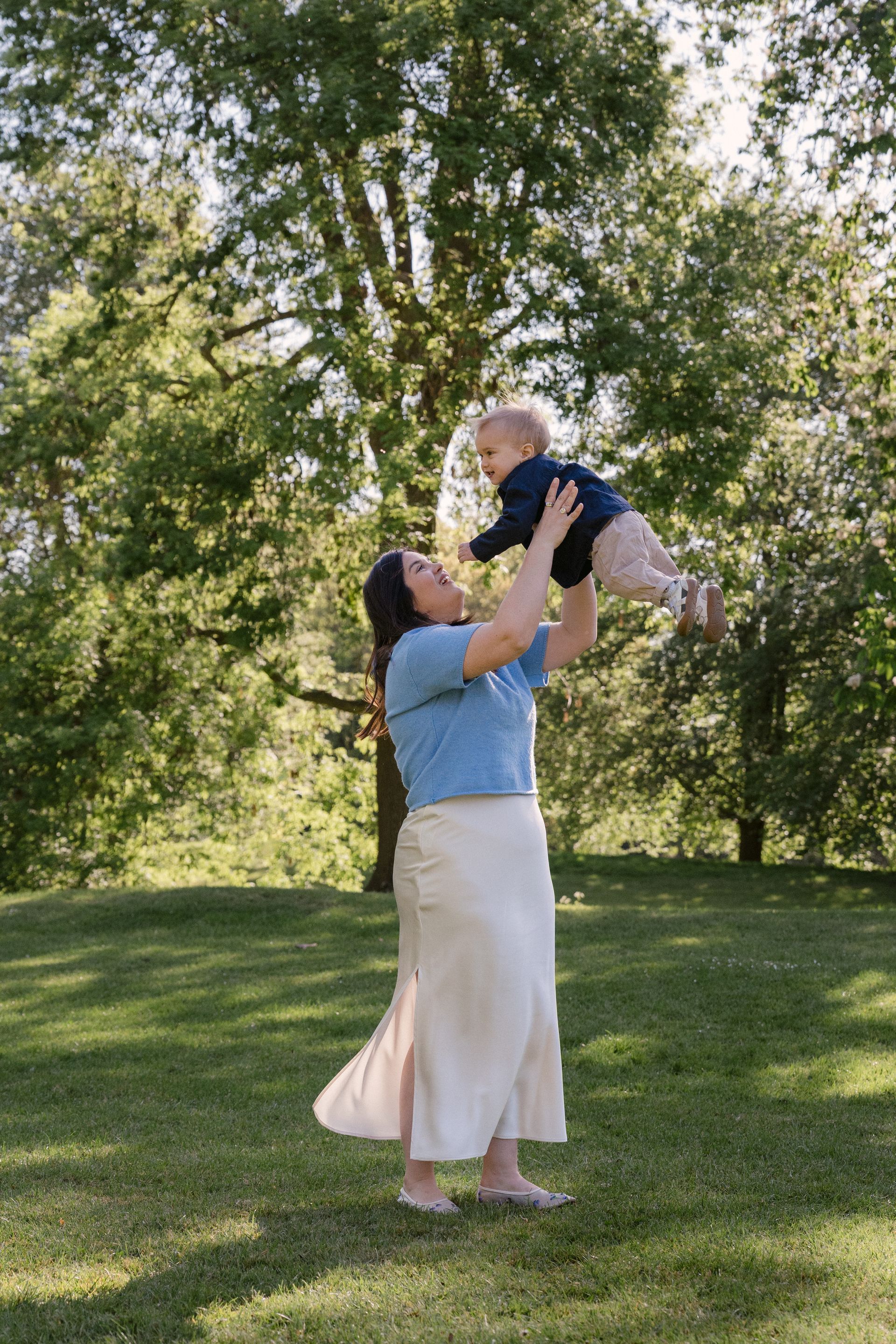A mother lifting her baby in a sunlit Regent's Park, London, during a family session