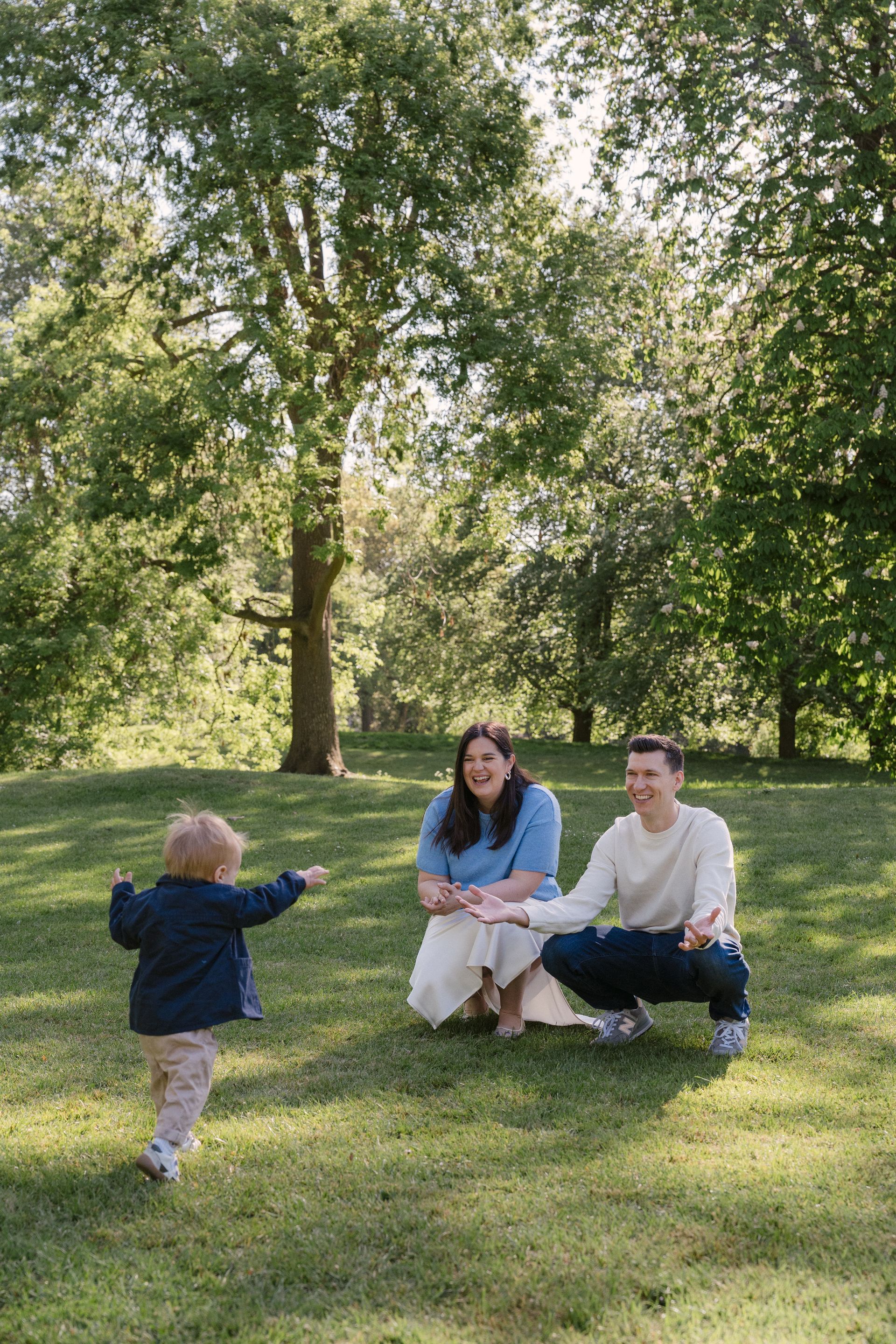 A small child running across the grass to their waiting parents in Regent's Park, London