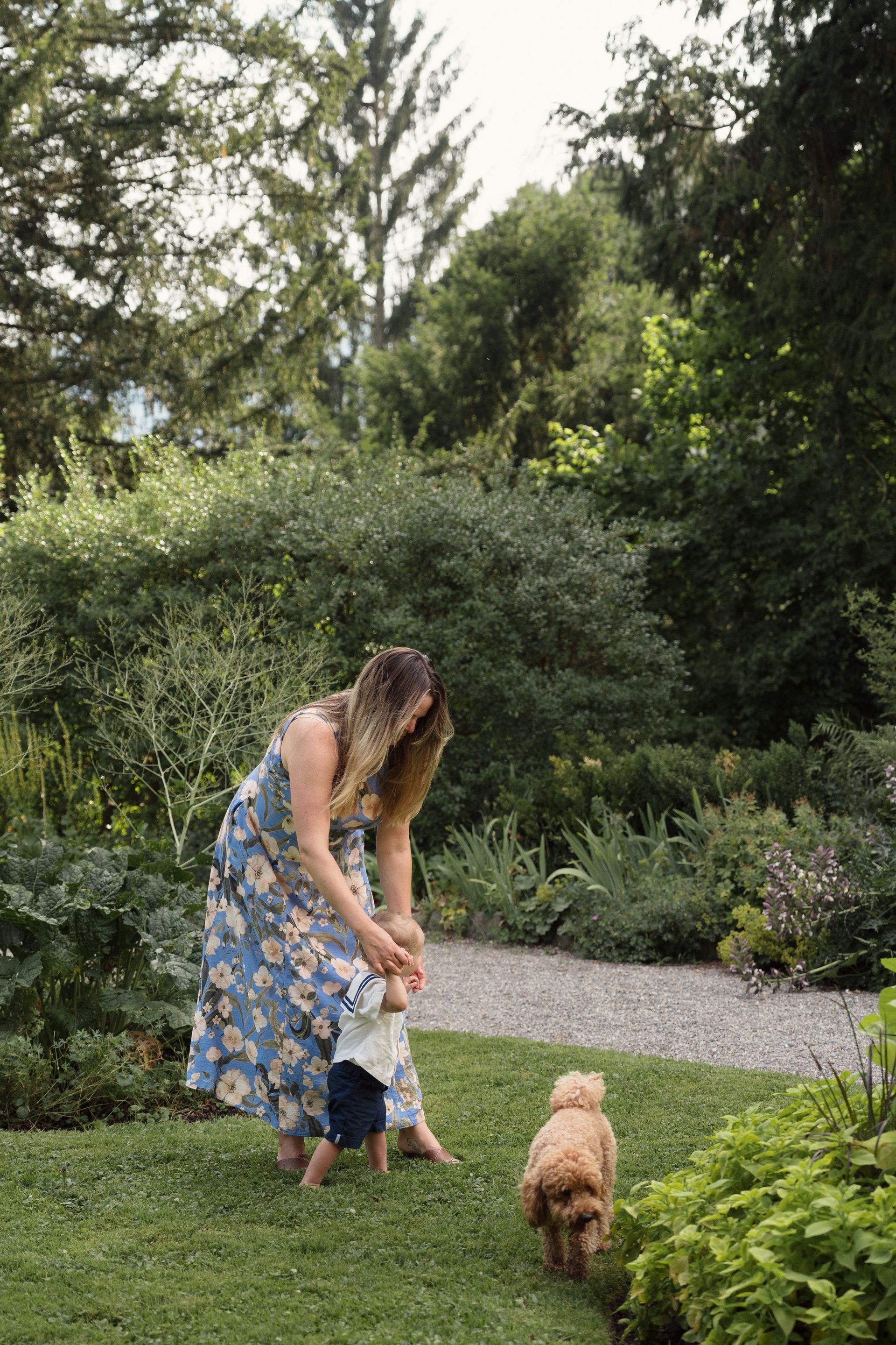 A mother in a floral dress walking her son and a small dog in the garden of Villa Patumbah, Zürich
