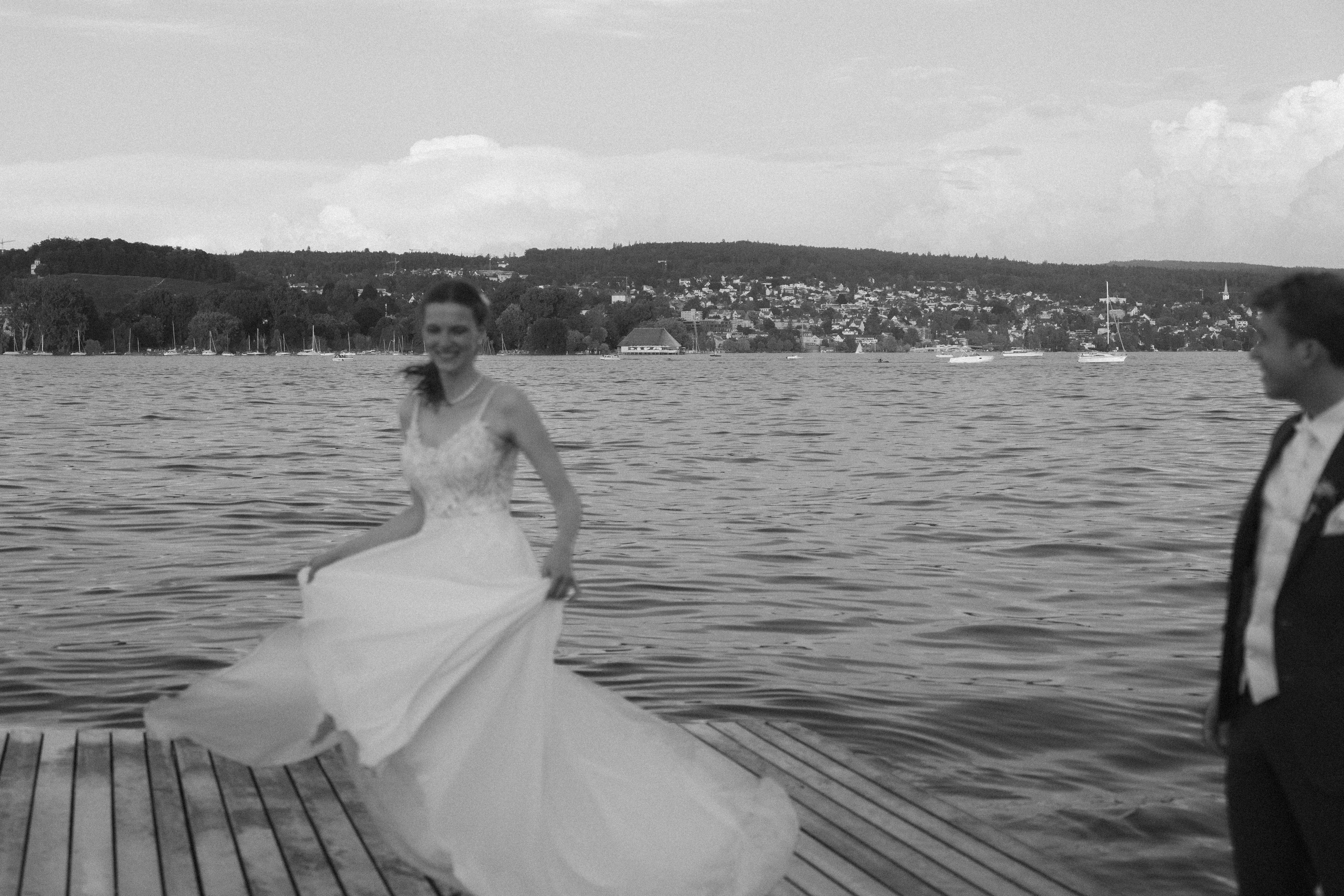 A bride dancing on a wooden lake jetty at sunset, the groom looking at her