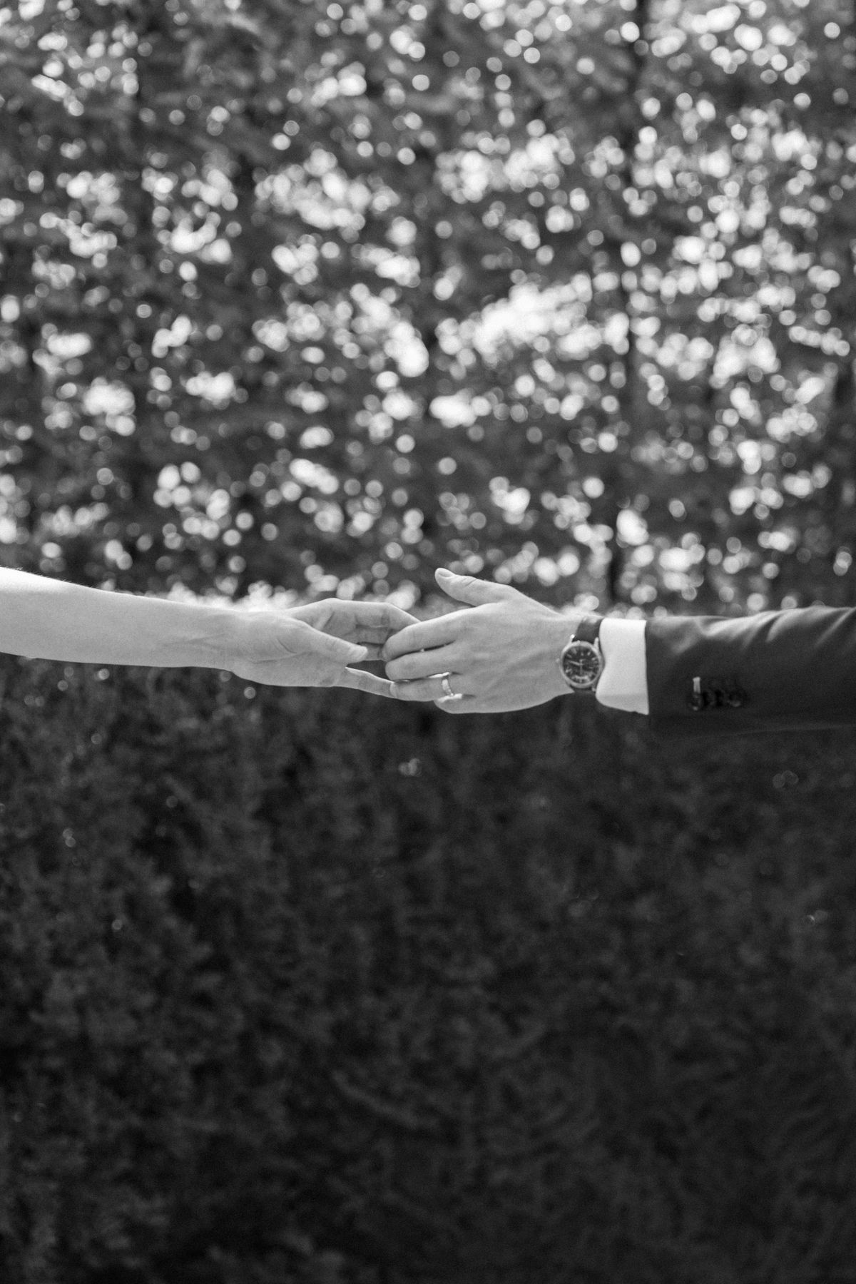A bride and groom reaching for each other's hands, in black and white